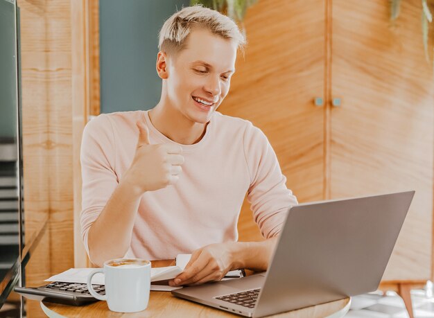 Gelukkig zakenman zit op cafetaria met laptop en smartphone. Zakenman texting op slimme telefoon zittend in een café, werken en e-mail controleren op computer