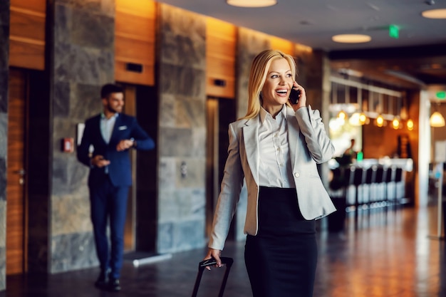 Gelukkig zakenvrouw op zakenreis wandelen in de hal van het hotel en praten over de telefoon. Luxe, zaken, telecommunicatie, zaken eerst, euforie