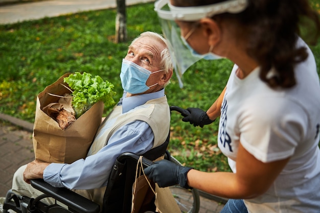 Gelukkig zelfverzekerde man in blauw shirt in rolstoel die tijd doorbrengt met vrouwelijke vrijwilliger