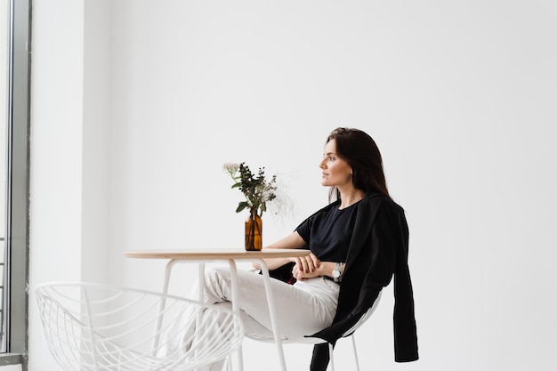 Gelukkig zelfverzekerde vrouw zit aan tafel op witte achtergrond binnen in café Lachende jonge vrouw gekleed casual zakelijke stijl genieten van haar levensstijl