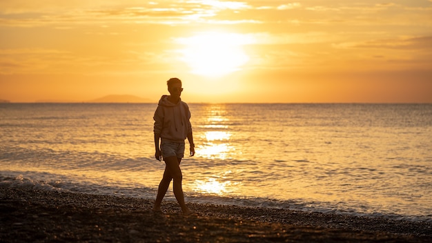 Gelukkig zorgeloze vrouw genieten van prachtige zonsopgang op het strand. Gele zon over zee. Oranje kleuren golven. Natuur achtergrond. Mooie serene scène. Ochtend.