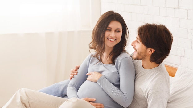 Gelukkig zwanger echtpaar ontspant zich samen in bed thuis.