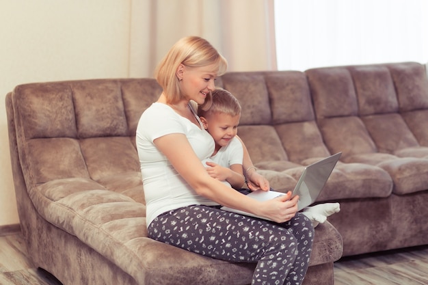 Gelukkig zwangere moeder met haar jongen die laptop thuis in de woonkamer gebruikt