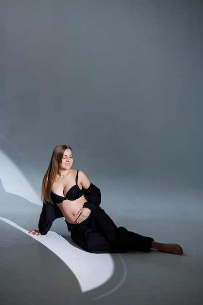 Gelukkig zwangere vrouw in een zwart pak op een grijze achtergrond Mooie elegante zwangere vrouw Gentle studio foto's van een zwangere vrouw