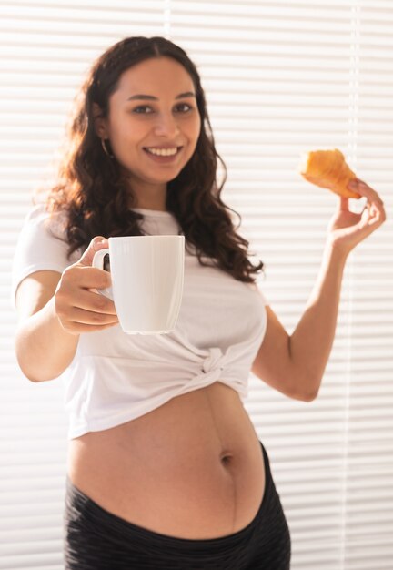 Gelukkig zwangere vrouw met croissant broodjes thuis zwangerschap eten en mensen concept