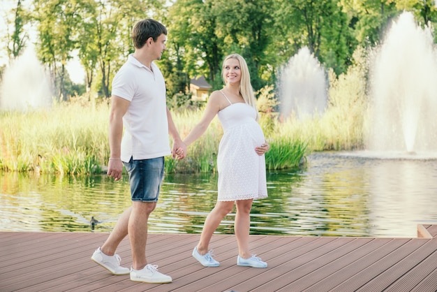 Gelukkig zwangere vrouw wandelen met man op pier in de buurt van het water in de avond. Vrije tijd buiten.