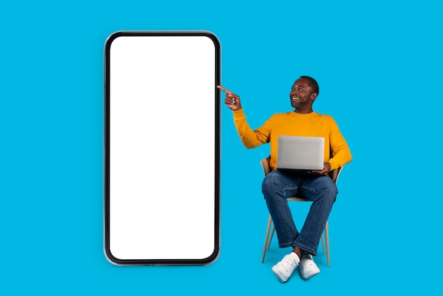 Gelukkig zwarte man freelancer met behulp van computer wijzend op smartphone mockup