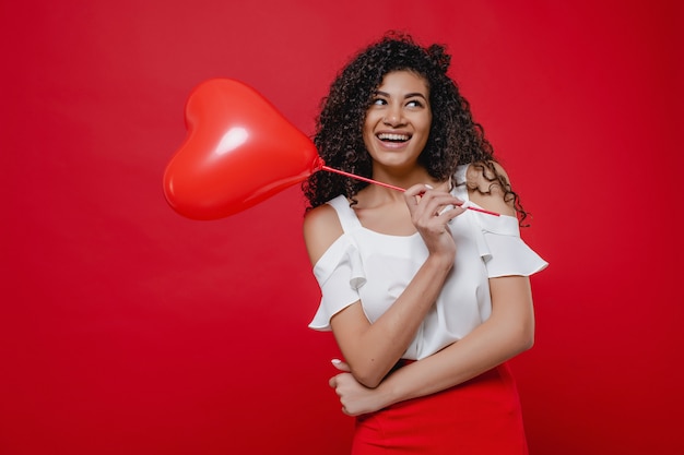 Gelukkig zwarte met hartvormige ballon die rok draagt die op rode muur wordt geïsoleerd