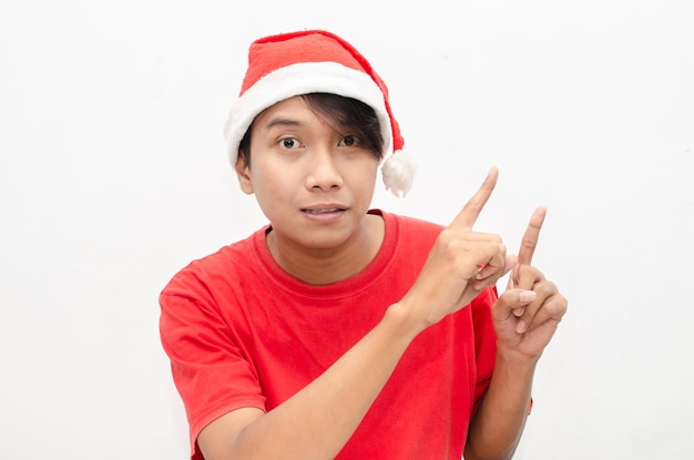 gelukkige aantrekkelijke Aziatische man in rode kerstkleding die met de vinger wijst en iets presenteert.