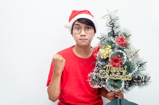 gelukkige aantrekkelijke Aziatische man in rode kerstthema-kleding terwijl hij de kerstboom vasthoudt.