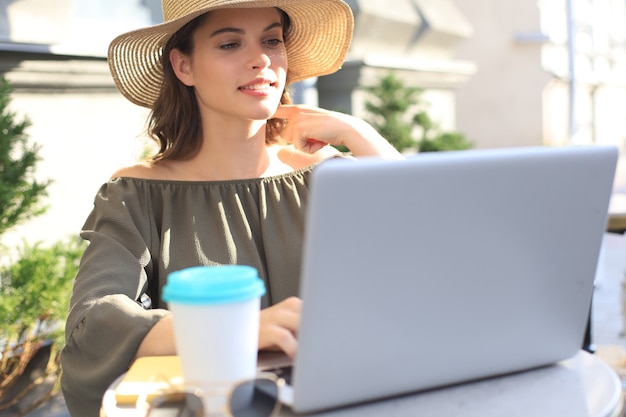 Gelukkige aardige vrouw die aan laptop in straatkoffie werkt.