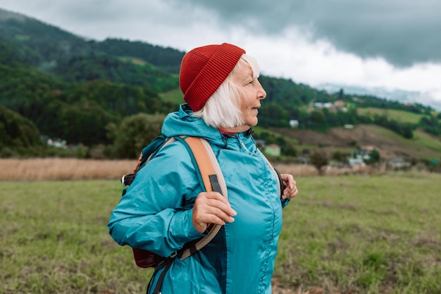 Gelukkige actieve oudere toeristische vrouw die naar muziek luistert tijdens een vakantie in de buitenlucht en het landschap bewondert