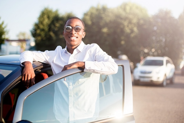 Gelukkige Afrikaanse Amerikaan naast een auto in de zomer