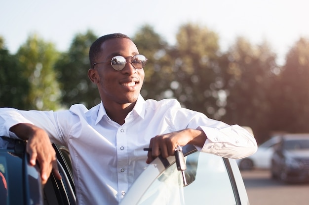 Gelukkige Afrikaanse Amerikaan naast een auto in de zomer