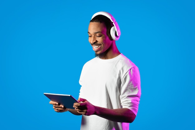 Gelukkige Afrikaanse kerel die digitale tablet en hoofdtelefoons gebruikt