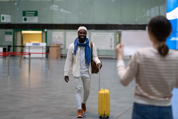 Gelukkige Afrikaanse man-werknemer met bagage die naar een vrouw gaat die op hem wacht met bord op de luchthaven