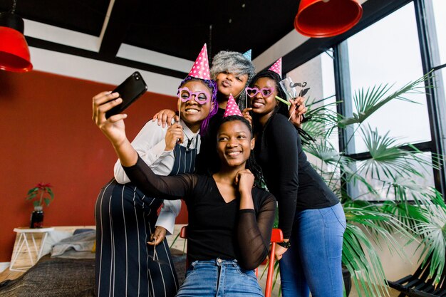 Gelukkige Afrikaanse meisjes vieren verjaardag in hoeden en nemen foto's op een smartphone