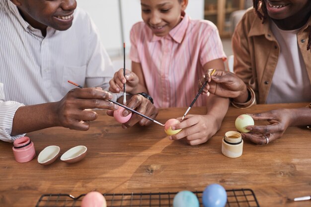 Gelukkige Afro-Amerikaanse familie die paaseieren samen schildert terwijl ze aan een houten tafel zitten en zich hecht aan een doe-het-zelf-project, kopieer ruimte