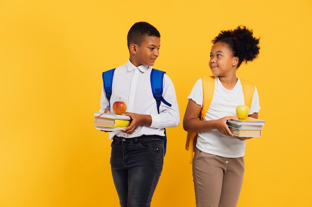 Gelukkige Afro-Amerikaanse schoolmeisje en schooljongen met boeken naast elkaar op gele achtergrond