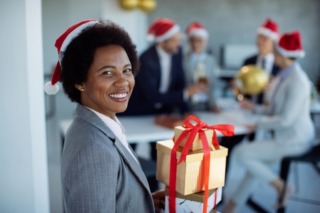 Gelukkige Afro-Amerikaanse zakenvrouw die kerstcadeautjes brengt op kantoorfeest