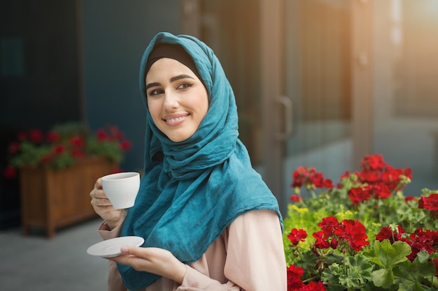 Gelukkige arabische vrouw in hijab die koffie drinkt in café buiten, kopieer ruimte