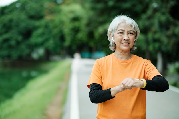 Gelukkige atletische Senior vrouw die haar smartwatch in het park controleert