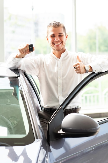 Foto gelukkige autobezitter toont duimen en zijn nieuwe autosleutel