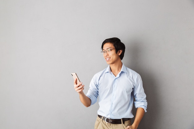 Gelukkige aziatische bedrijfsmens die zich geïsoleerd bevindt, die mobiele telefoon houdt, golvend