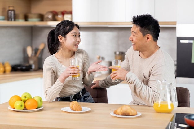 Gelukkige Aziatische echtgenoten die plezier hebben tijdens het eten in de keuken