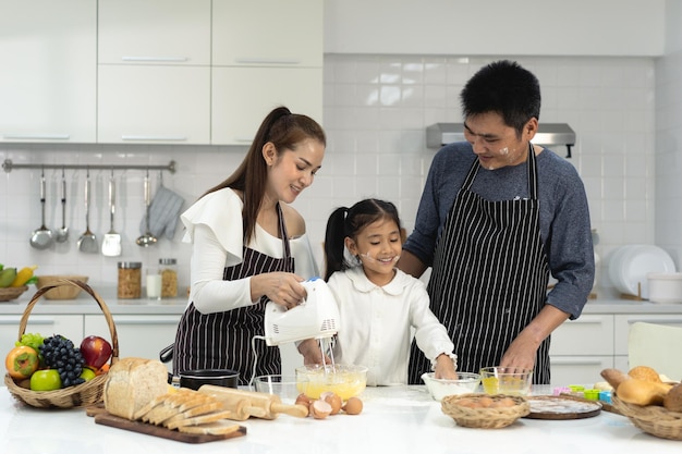 Gelukkige Aziatische familie met dochter die deeg maakt om koekjes te bakken Dochter helpt ouder bij het voorbereiden van het bakgezin Familieconcept