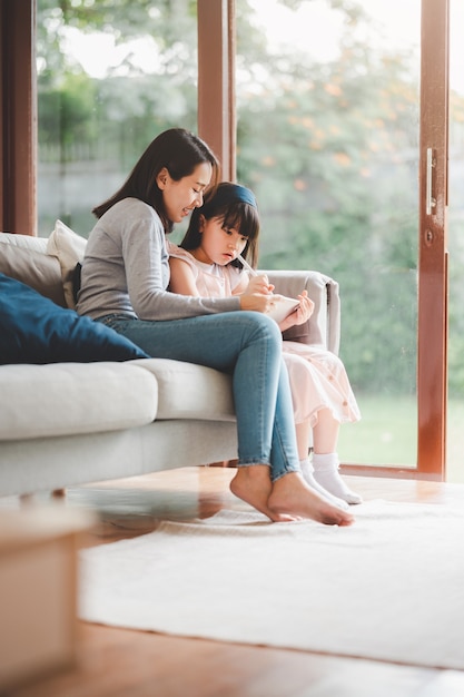 Gelukkige Aziatische familiemoeder en dochter die digitale tablet gebruiken om thuis samen te studeren.