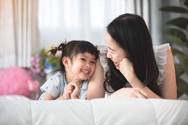 Gelukkige aziatische familiemoeder met dochter het spelen op bed met glimlachgezicht