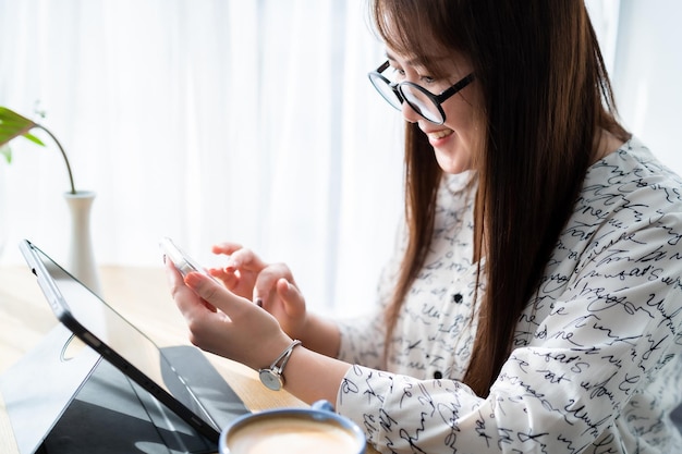 Gelukkige aziatische freelance mensen zakelijke vrouw schrijven bericht op smartphone werken casual werken met tablet voor browsen op internet chatten en bloggen met koffiekopje in coffeeshop