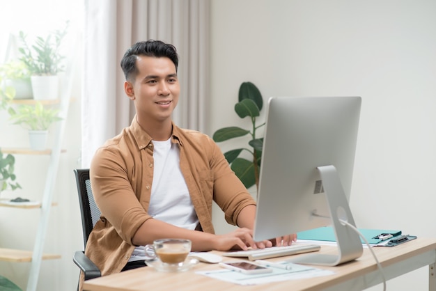 Gelukkige Aziatische freelancer man werkt op zijn computer