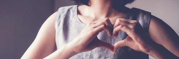 Gelukkige Aziatische jonge vrouw die haar maken hartvorm indient