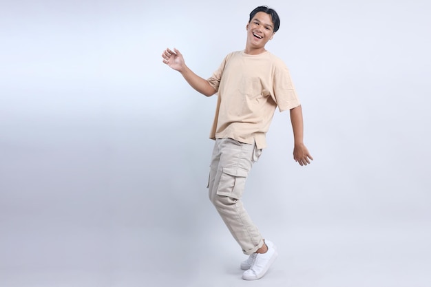 Gelukkige Aziatische man die op zijn favoriete liedje danst en op zijn tenen staat, geïsoleerd over een witte achtergrond.