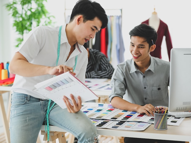 Gelukkige Aziatische mannen glimlachen en onderzoeken schetsen over stofmonsters terwijl ze in atelier werken