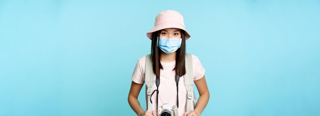 Gelukkige aziatische meisjestoerist die zich in een medisch gezichtsmasker bevindt en camera vasthoudt die foto's maakt tijdens vakantie
