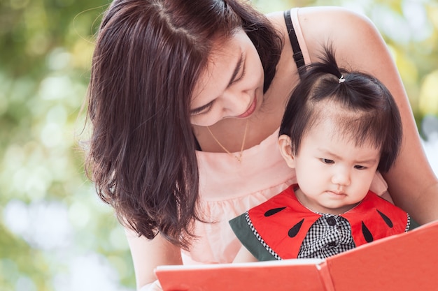 Gelukkige Aziatische moeder en leuk klein babymeisje die een boek samen met pret en liefde lezen