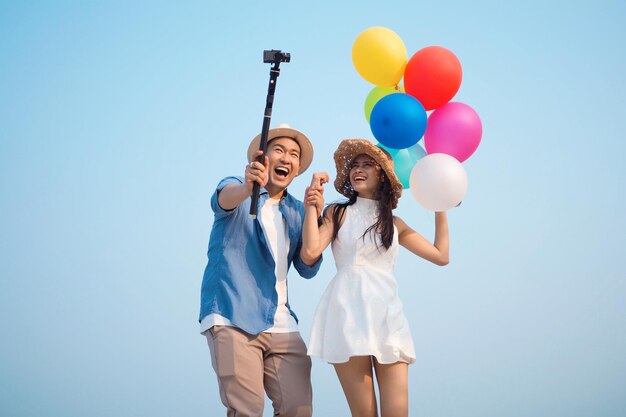 Gelukkige Aziatische paar selfie-foto's samen met kleurrijke ballonnen aan zee