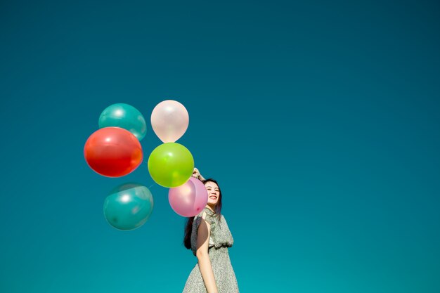 Gelukkige Aziatische vrouw die kleurrijke ballons op blauwe hemel speelt. Vrijheid concept