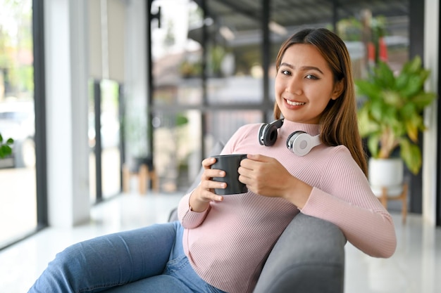 Gelukkige Aziatische vrouw die koffie drinkt terwijl ze ontspant in de moderne coffeeshop