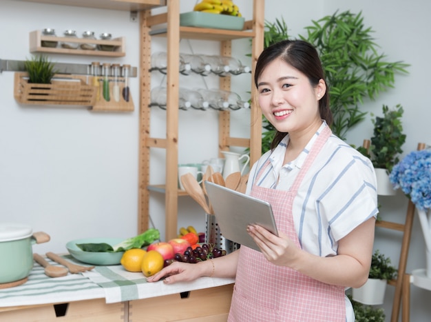 Gelukkige Aziatische vrouw die recept in de keuken maakt