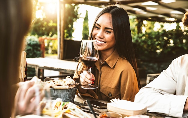 Gelukkige aziatische vrouw die rode wijn drinkt die aan de eettafel van het restaurant zit