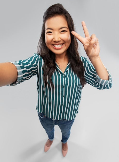 Gelukkige Aziatische vrouw die selfie neemt en vrede toont