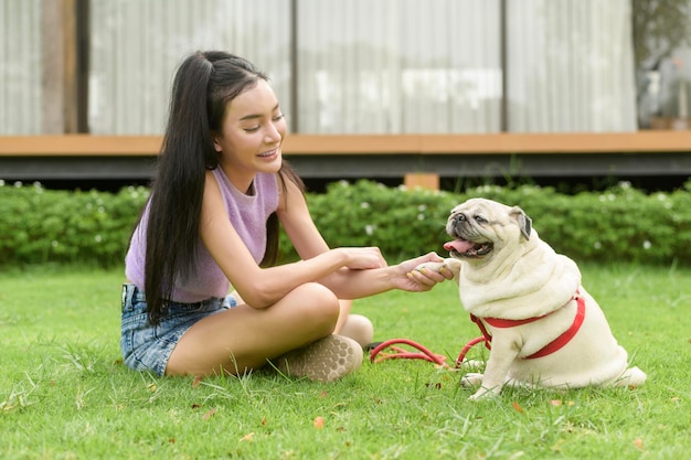 Gelukkige Aziatische vrouw speelt met schattige slimme pug puppy hond in de achtertuin