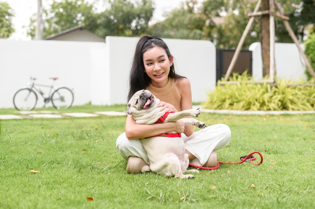 Gelukkige Aziatische vrouw speelt met schattige slimme pug puppy hond in de achtertuin