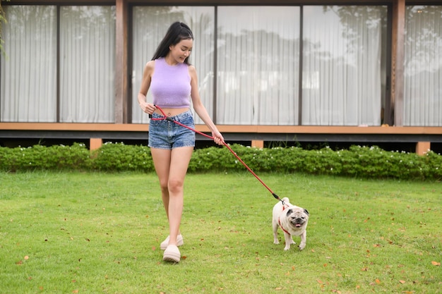 Gelukkige Aziatische vrouw speelt met schattige slimme pug puppy hond in de achtertuin