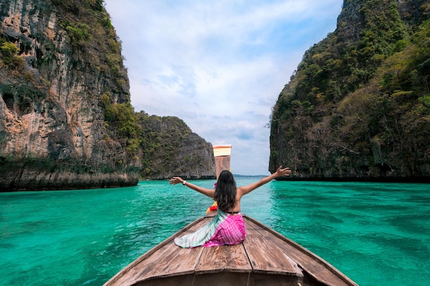gelukkige Aziatische vrouwelijke reiziger zit op een boot met lange staart en kijkt naar de prachtige natuurlijke Pileh-lagune Krabi op het eiland Phi Phi. zee reizen Phuket Thailand, toeristische meisje ontspannen op zomervakantie.