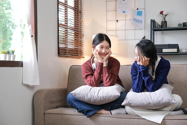 Gelukkige Aziatische vrouwelijke vrienden thuis zittend op de Bank twee jonge vrouwen met chatten op de bank roddelen en delen van geheimen bespreken leven en relaties vriendschap vertrouwen concept